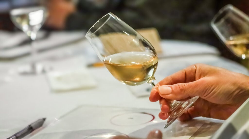 Professional sommelier swirling and closely observing a glass of white wine during a wine tasting session, meticulously assessing its color, clarity, and captivating aroma