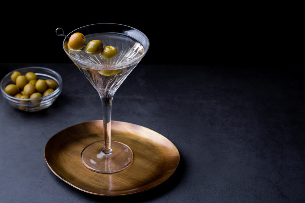 Dirty martini cocktail in back light with olives garnish on dark stone table, top view, copy space